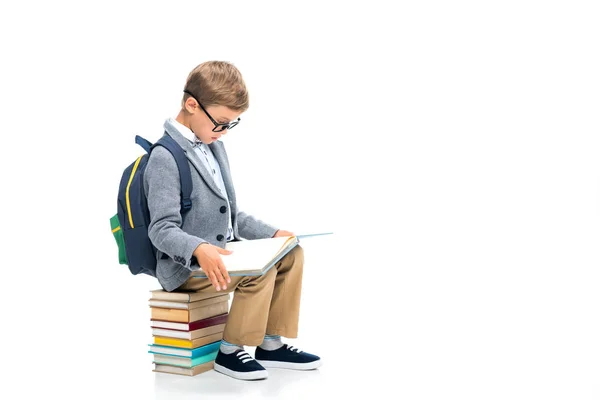 Schoolboy sittting on stack of books and reading — Stock Photo