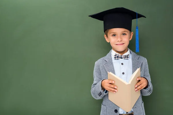 Écolier en chapeau de graduation et avec livre — Photo de stock