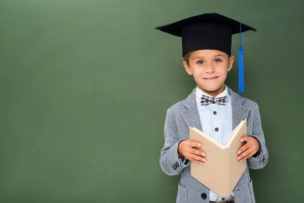 Colegial en sombrero de graduación y con libro - foto de stock