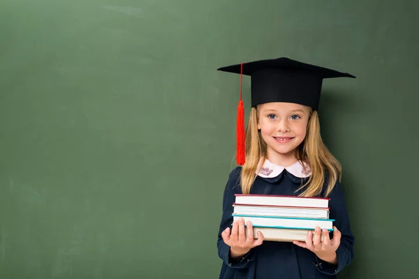 Écolière avec pile de livres et chapeau de graduation — Photo de stock