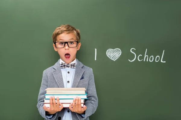 Shocked schoolboy with stack of books — Stock Photo