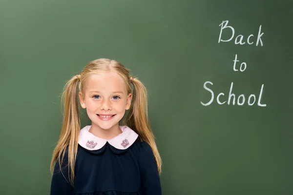 Happy schoolgirl next to chalkboard — Stock Photo