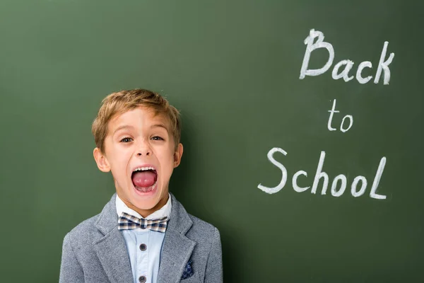 Sreaming schoolboy next to chalkboard — Stock Photo