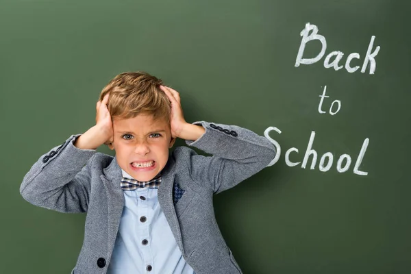 Angry schoolboy holding his head — Stock Photo