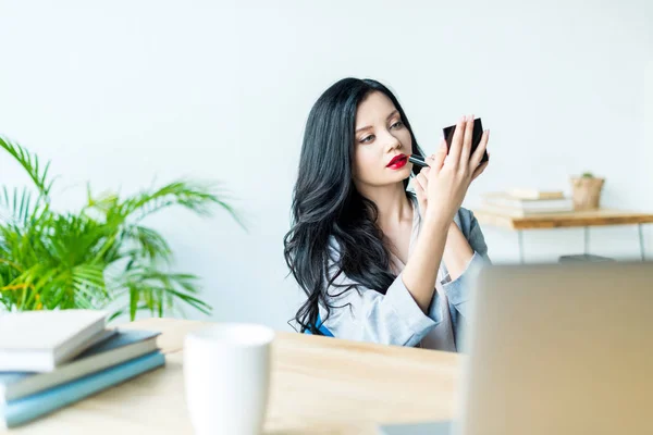 Donna d'affari che applica rossetto sul posto di lavoro — Foto stock