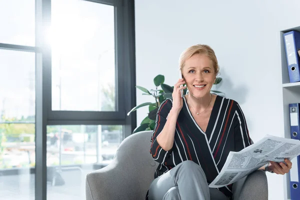 Businesswoman with newspaper talking by phone — Stock Photo