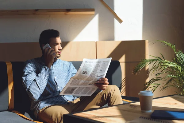 Man with smartphone reading newspaper — Stock Photo