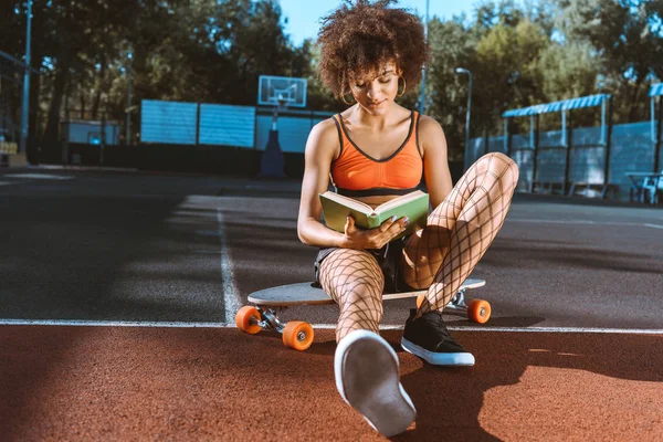 Mujer afroamericana en libro de lectura longboard - foto de stock