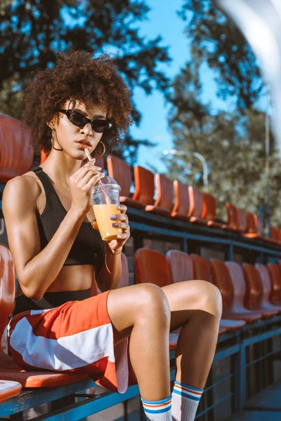 African-american woman in bleachers with juice — Stock Photo