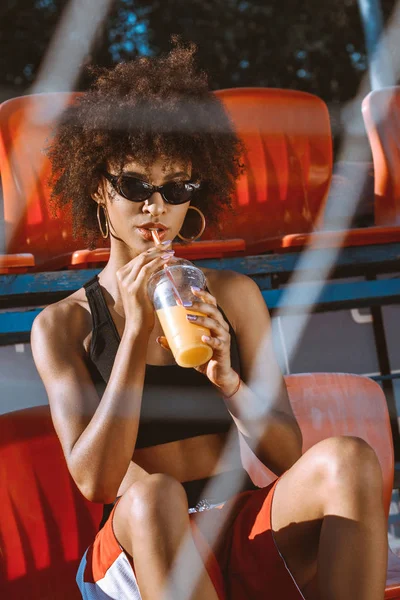 Mulher afro-americana em arquibancadas beber suco — Fotografia de Stock