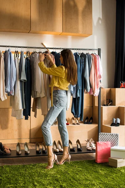 Mujer joven eligiendo ropa en boutique - foto de stock