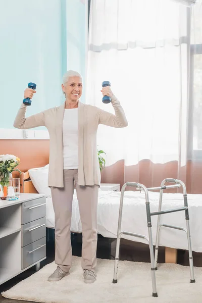 Senior woman with dumbbells in hospital — Stock Photo