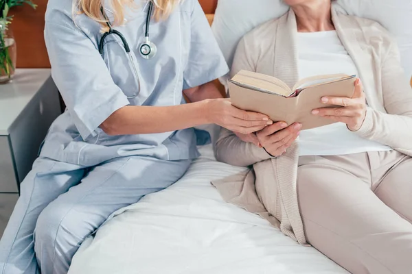 Медсестра і старший пацієнт з книгою — стокове фото