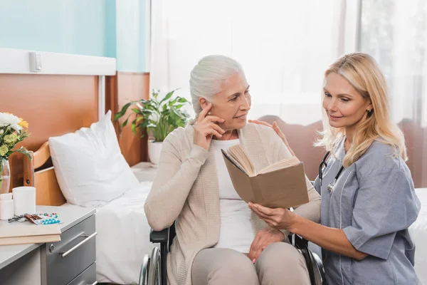Infirmière et patiente âgée avec livre — Photo de stock