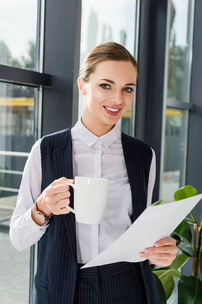 Mujer de negocios sosteniendo taza y papeles - foto de stock