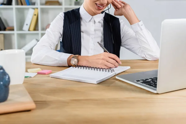Businesswoman with headset taking notes — Stock Photo