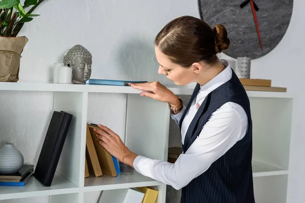 Geschäftsfrau betrachtet Bücher im Regal — Stockfoto