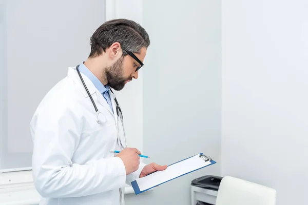 Médecin concentré regardant le presse-papiers — Photo de stock