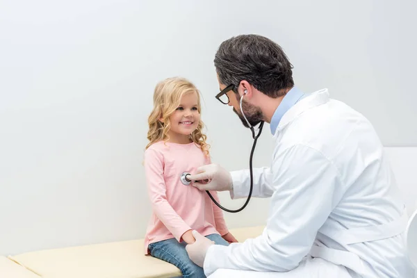 Pediatra escuchando el aliento de una niña - foto de stock