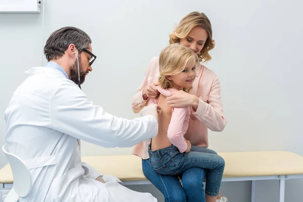 Pediatra escuchando el aliento de una niña - foto de stock