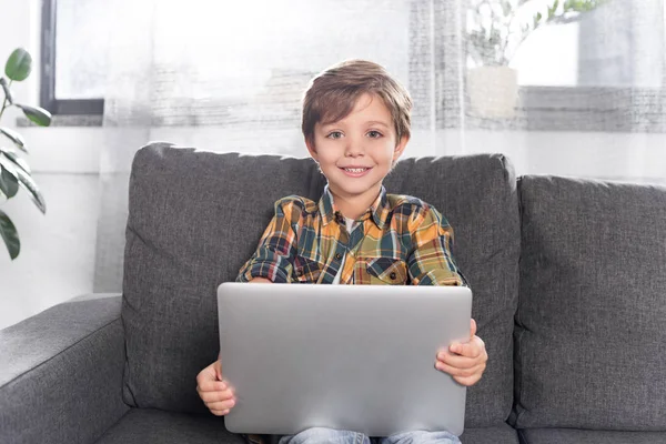 Niño con portátil sentado en el sofá - foto de stock