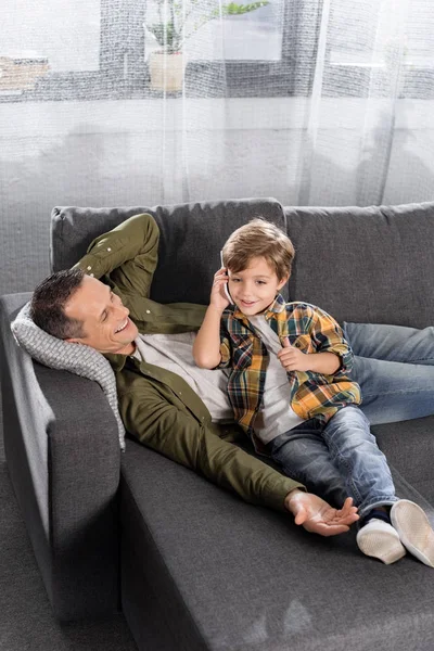 Bambino che parla per telefono mentre il padre riposa — Foto stock