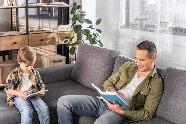 Pai com livro e filho com tablet — Fotografia de Stock