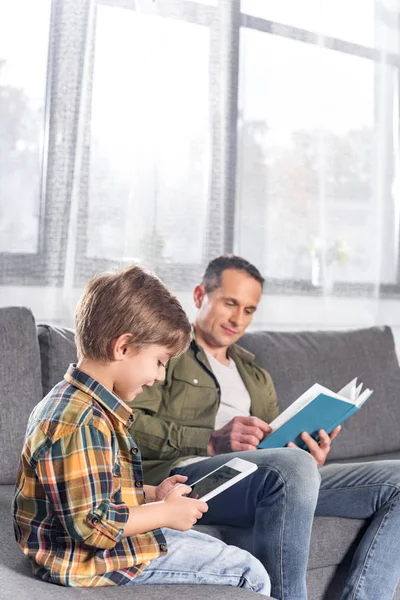 Vater mit Buch und Sohn mit Tablet — Stockfoto