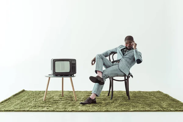 Homme en lunettes de soleil et costume sur chaise avec tv — Photo de stock