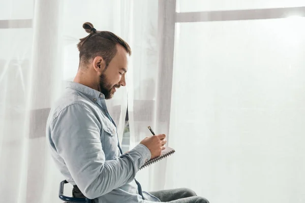 Man writing in notebook in front of window — Stock Photo