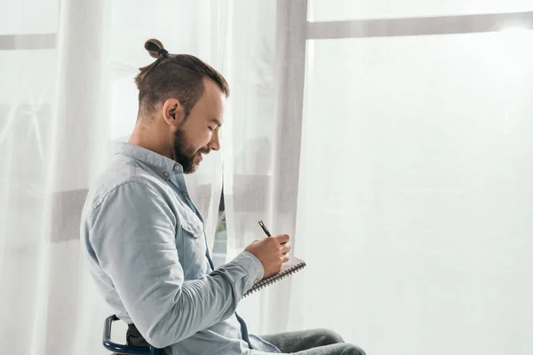 Hombre escribiendo en cuaderno delante de la ventana - foto de stock