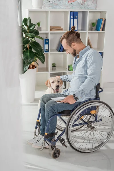 Uomo sulla sedia a rotelle accarezzare il suo cane — Foto stock