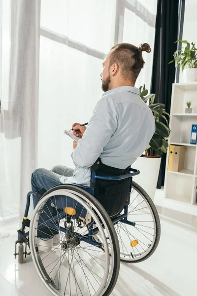 Man on wheelchair writing in notebook — Stock Photo