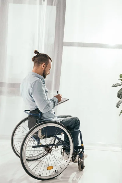 Man on wheelchair writing in notebook — Stock Photo