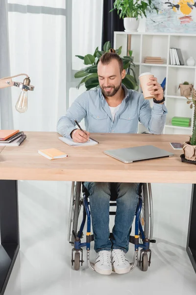 Uomo sulla sedia a rotelle seduto al tavolo da lavoro — Foto stock