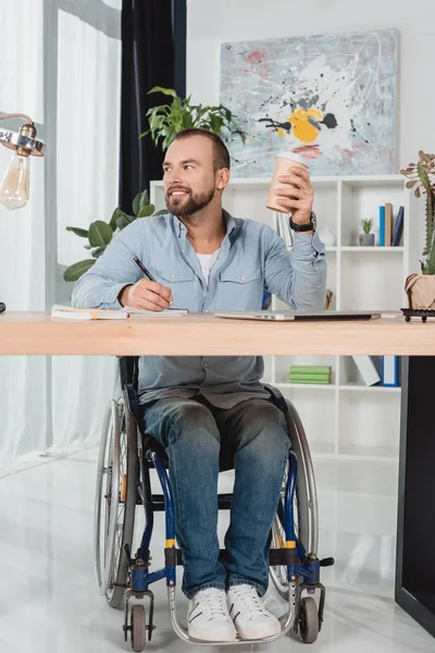 Hombre en silla de ruedas sentado en la mesa de trabajo - foto de stock