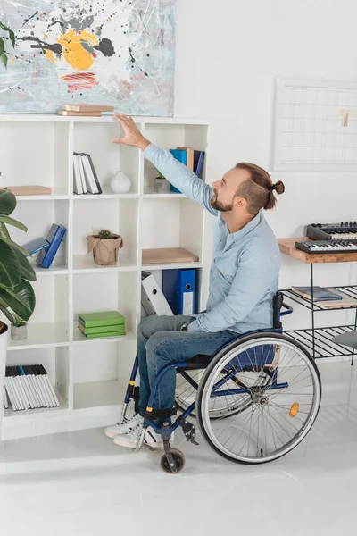 Мужчина на инвалидной коляске пытается дотянуться до книги — стоковое фото
