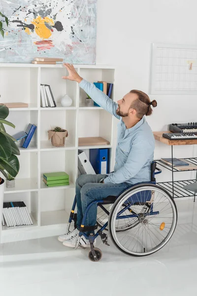 Hombre en silla de ruedas tratando de llegar a libro - foto de stock