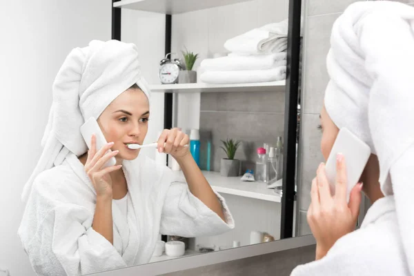 Frau spricht per Smartphone und putzt Zähne — Stockfoto