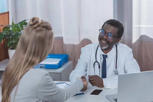 Médico y paciente estrechando las manos - foto de stock