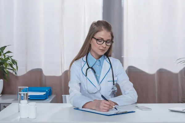 Doctor escribiendo algo en el portapapeles - foto de stock