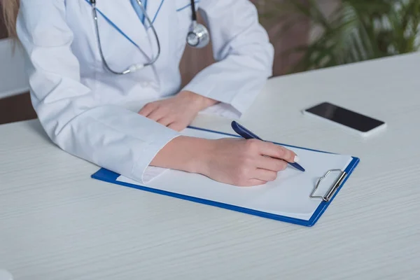 Doctor escribiendo algo en el portapapeles - foto de stock