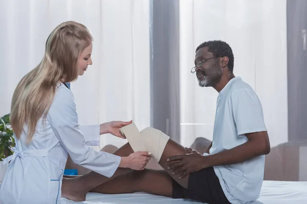 Доктор бинтование ноги пациента — стоковое фото
