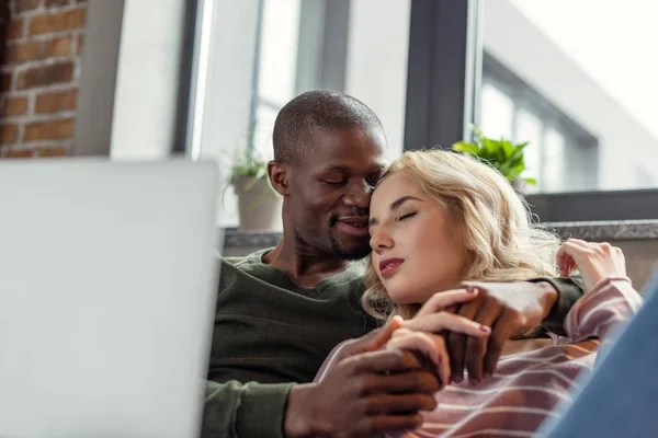 Enfoque selectivo de sensual afroamericano hombre abrazando novia mientras descansan en sofá juntos — Stock Photo
