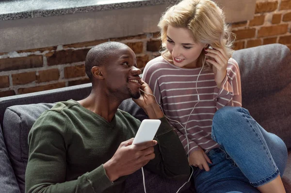 Feliz pareja multicultural en auriculares escuchando música juntos en casa - foto de stock