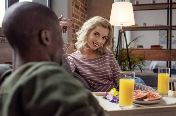 Vista parziale della donna sorridente che guarda il fidanzato afro-americano mentre fa colazione a casa — Foto stock