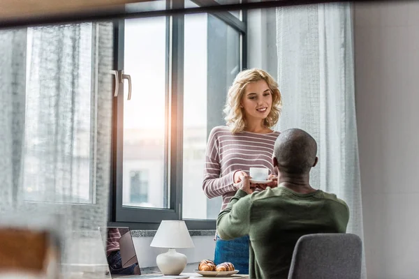 Girlfriend brought cup of coffee and croissants for african american boyfriend that working at home — Stock Photo