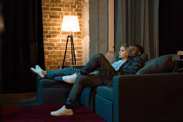 Vue latérale de jeune couple multiculturel regardant la télévision ensemble à la maison — Photo de stock
