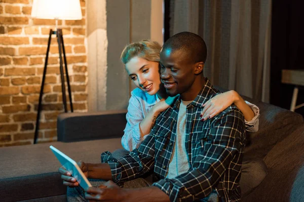 Multicultural couple using tablet together while resting on sofa at home — Stock Photo