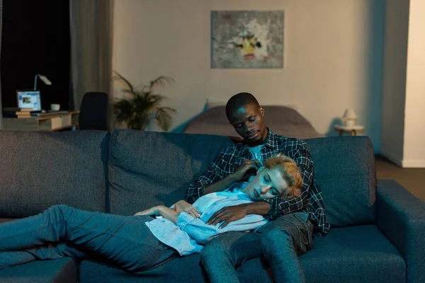 Афроамериканець людиною, дивлячись на подруга спати на колінах в домашніх умовах — стокове фото